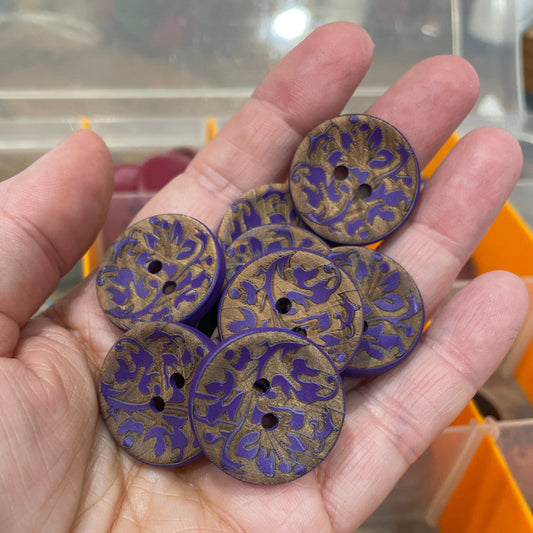 Hand holding five purple buttons with floral patterns against a blurred background