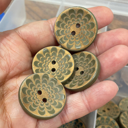 Hand holding decorative buttons with a container of similar buttons in the background