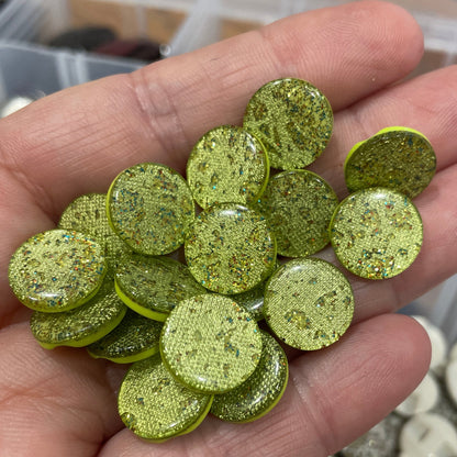 Hand holding green glittery buttons with a blurred background of more buttons.