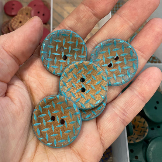 Hand holding decorative buttons with a container of assorted buttons in the background