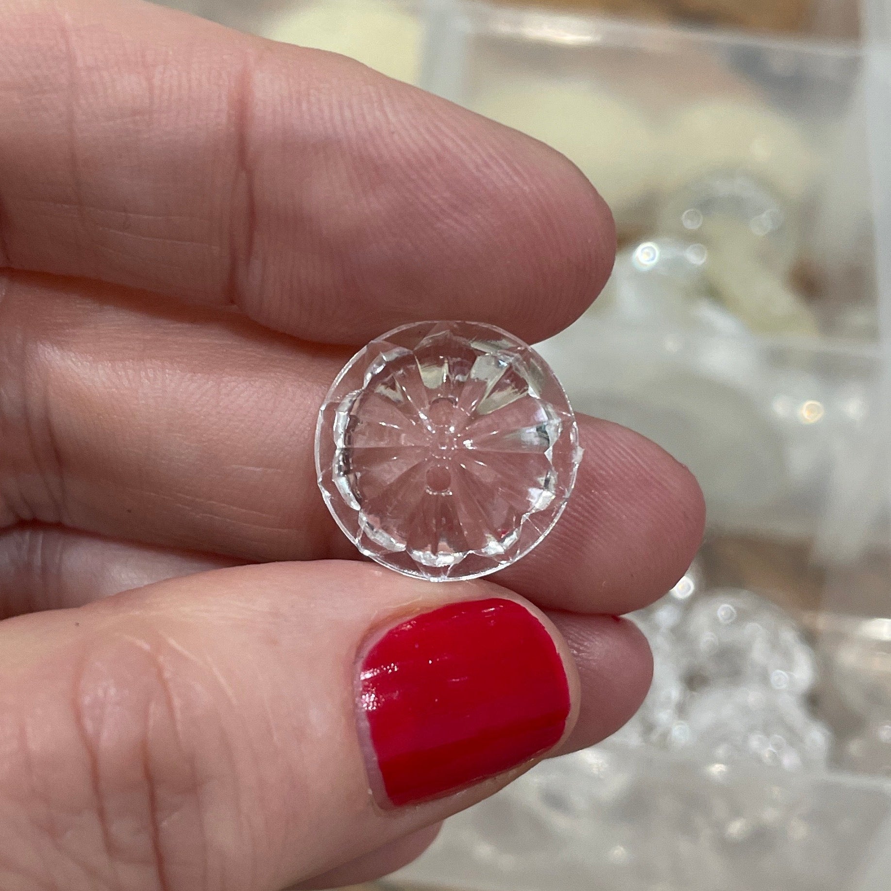 Hand holding a clear gemstone in front of a jewelry organizer.