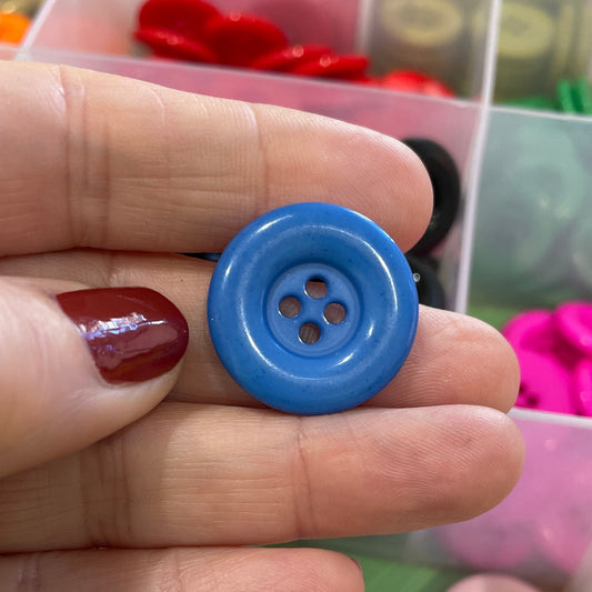 Hand holding a blue button with a container of colorful buttons in the background