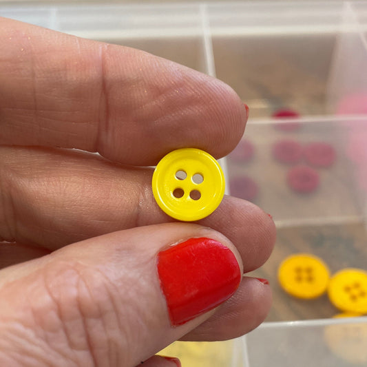Hand holding a yellow button with a clear container of buttons in the background