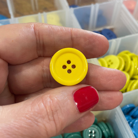 Hand holding a yellow button with a container of colorful buttons in the background