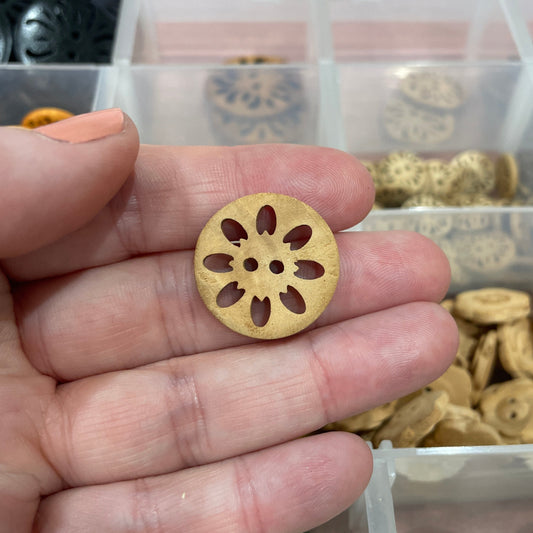 Hand holding a gold decorative button with a clear container of buttons in the background