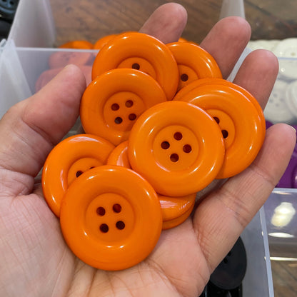 Hand holding orange buttons with a background of button assortment