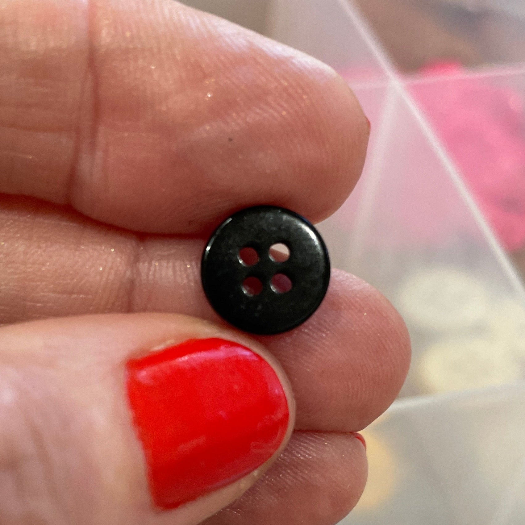 Hand holding a black button with a clear container of colorful buttons in the background