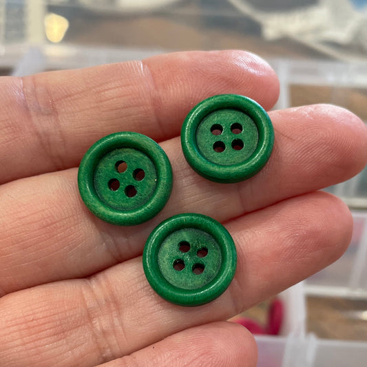 Three green buttons held between fingers with a container of buttons in the background.