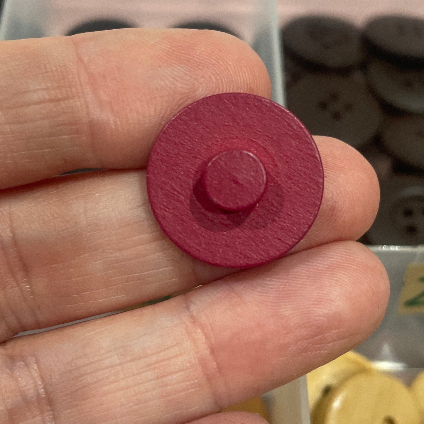 Hand holding a red button with a container of buttons in the background