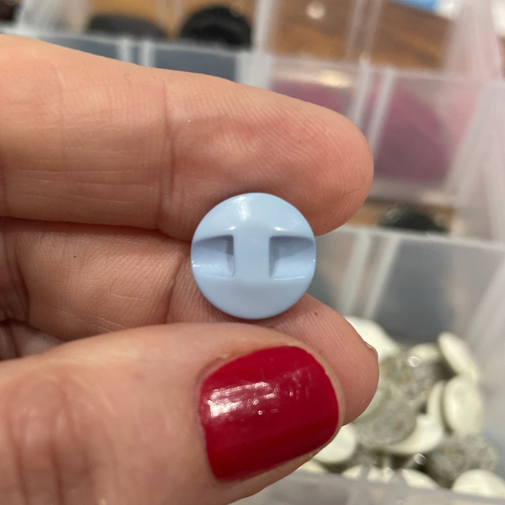 Hand holding a light blue button with a blurred background of colorful buttons in a box.