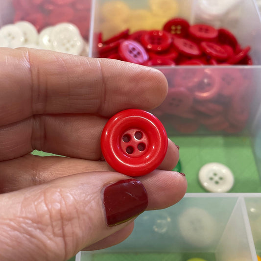Hand holding a red button with a background of variously colored buttons in clear containers.