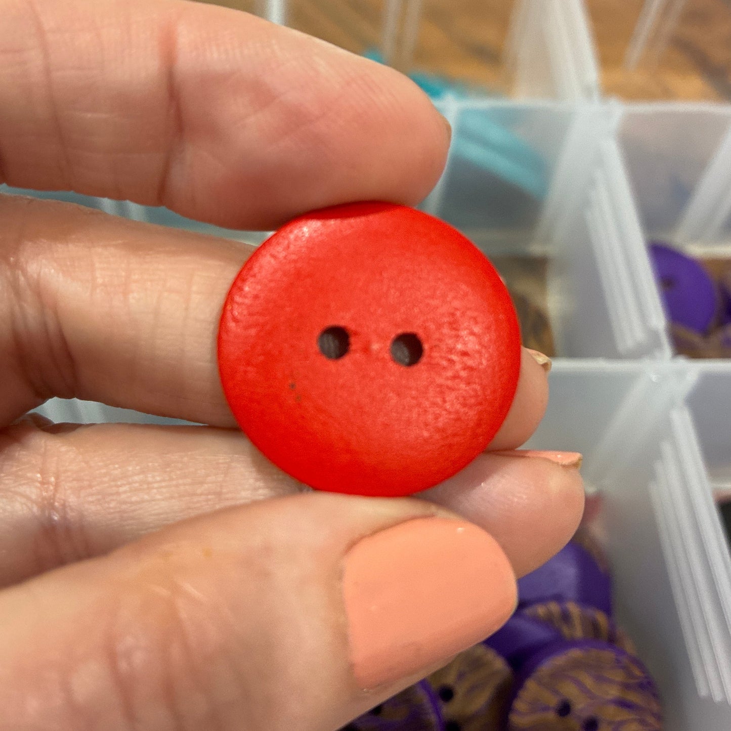 Hand holding a red button with a blurred background of a storage container with buttons.