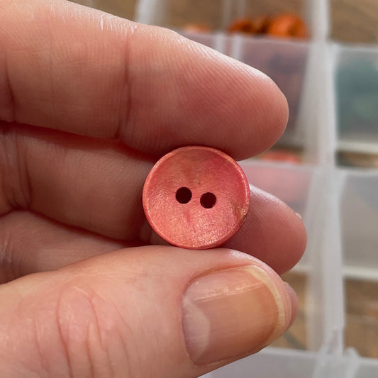Hand holding a pink button with a container of buttons in the background