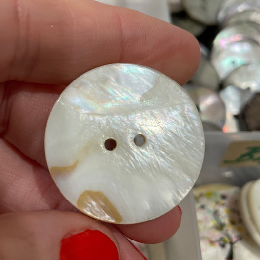 Hand holding a large decorative button with a blurred background of more buttons.