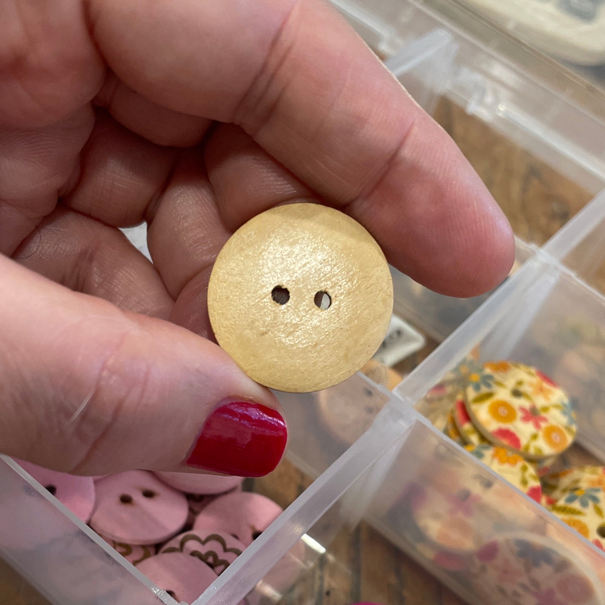 Hand holding a beige button with a container of colorful buttons in the background