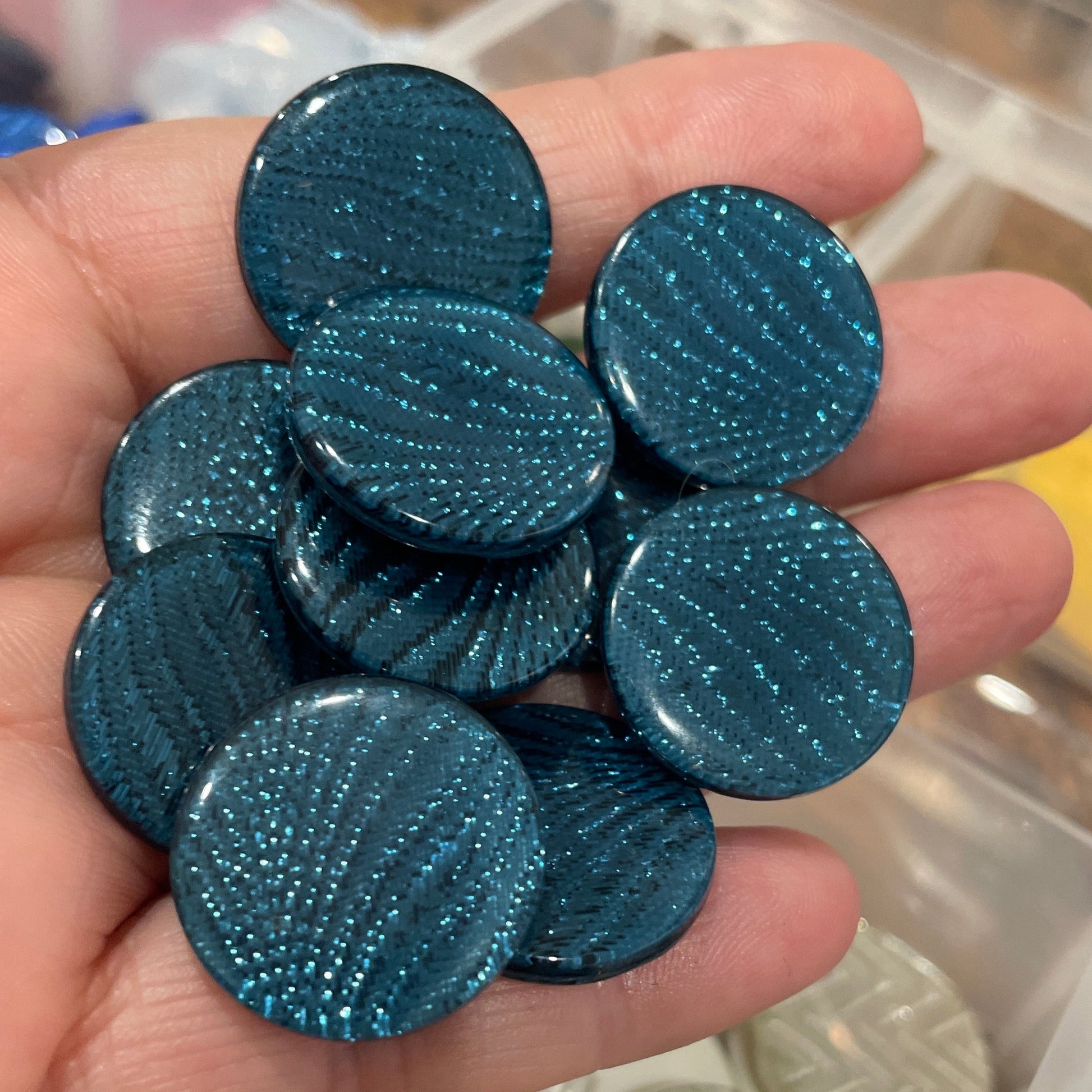 Hand holding blue circular objects with a container of similar objects in the background