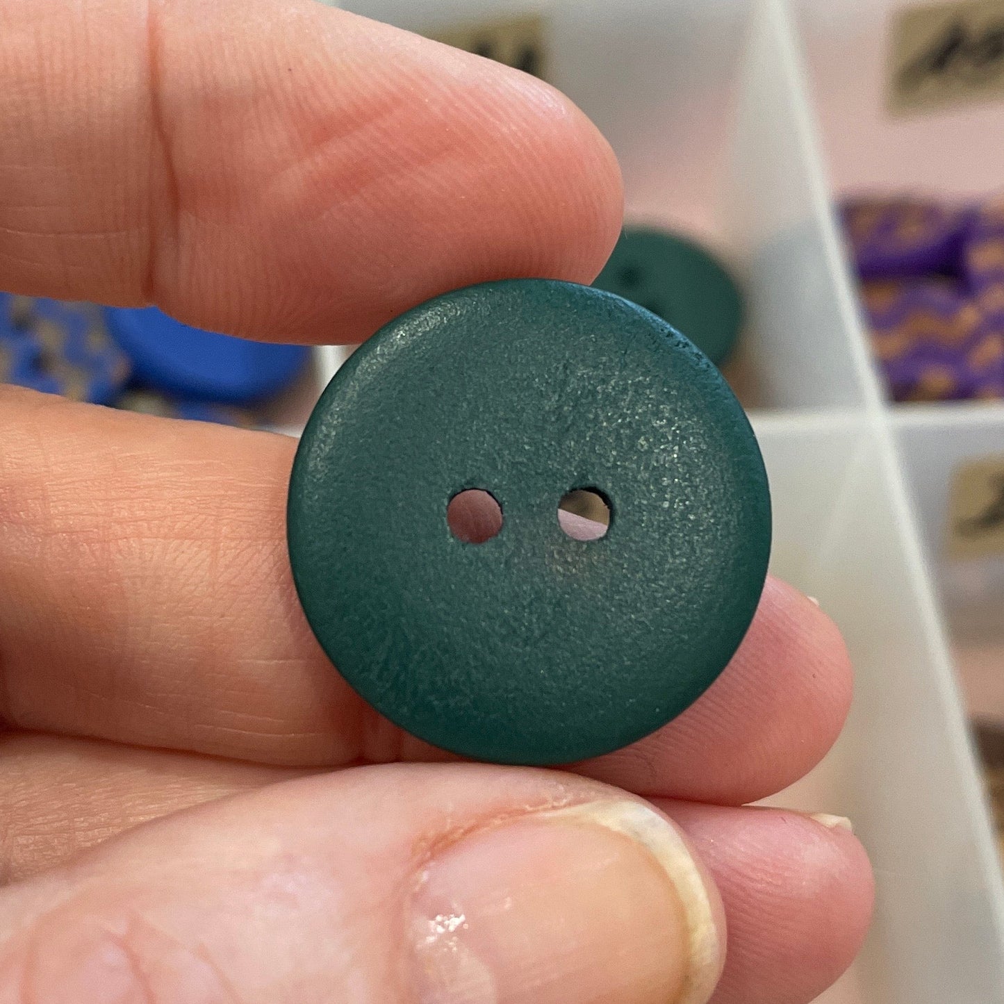 Hand holding a green button with a blurred background of a storage box with buttons.