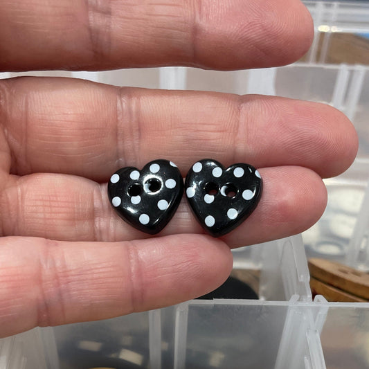 Hand holding black buttons with white dots next to a container of assorted buttons.