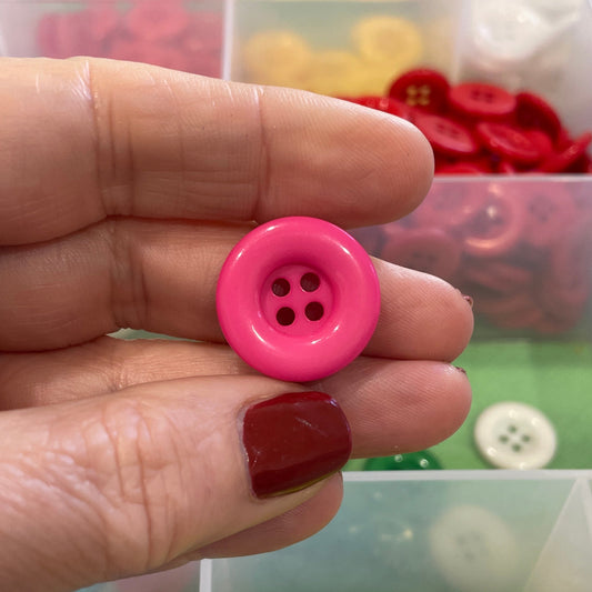 Hand holding a pink button with a colorful button collection in the background
