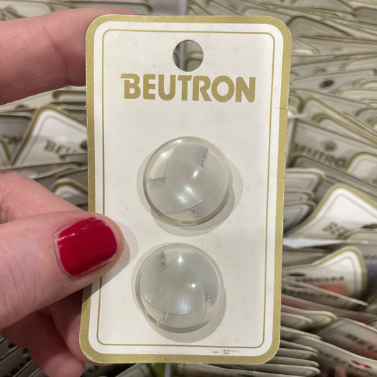 Two round buttons on a Beutron packaging with a hand holding it.