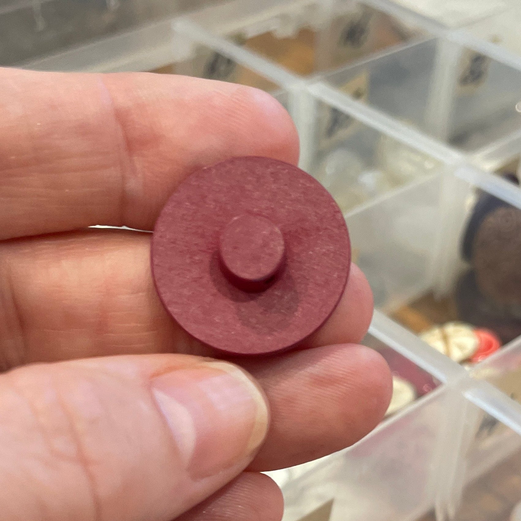 Hand holding a red button with a container of blue and pink objects in the background