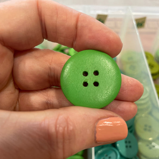 Hand holding a green button with a container of buttons in the background