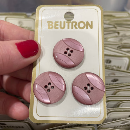 Three purple buttons on a Beutron card held by a hand with red nail polish.