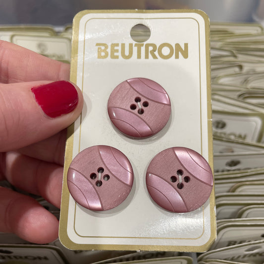 Three purple buttons on a Beutron card held by a hand with red nail polish.