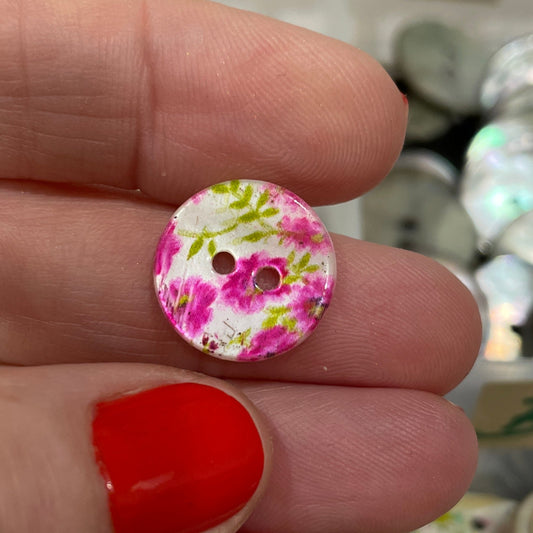 Hand holding a floral button with a blurred background of more buttons