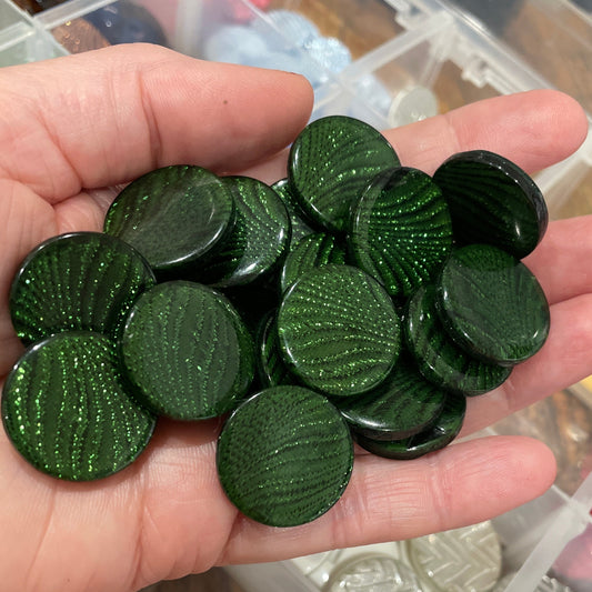 Hand holding green circular objects with a container of various buttons in the background