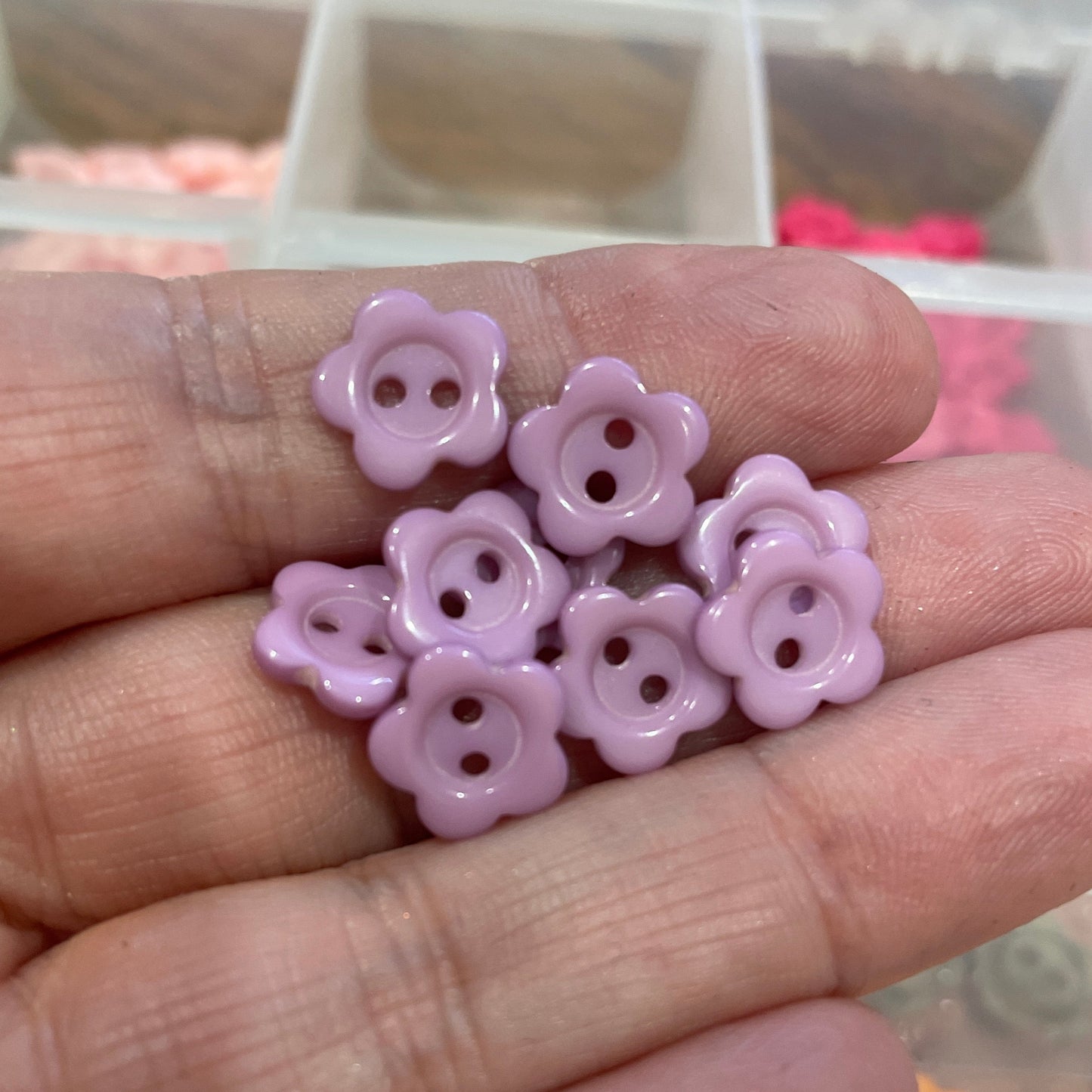 Hand holding pink flower-shaped buttons with a blurred background of more buttons.