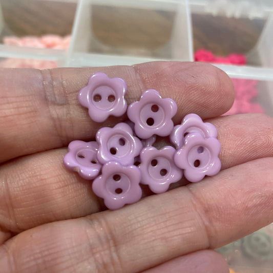 Hand holding pink flower-shaped buttons with a blurred background of more buttons.