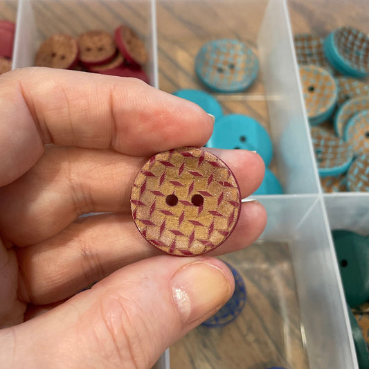 Hand holding a wooden button with a container of buttons in the background