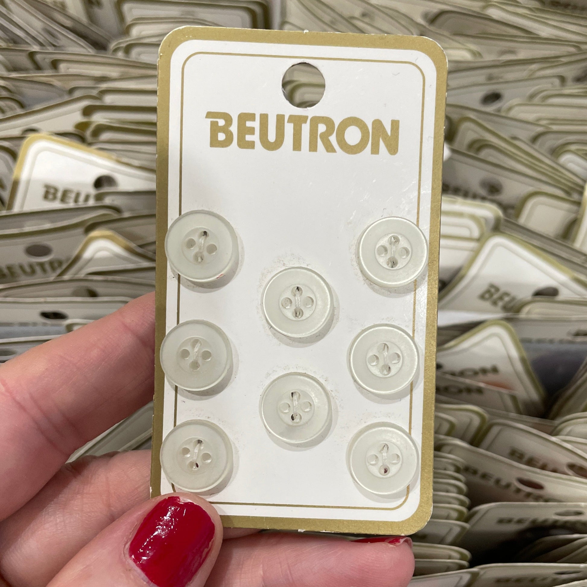 Hand holding a package of buttons with 'BEUTRON' branding against a background of similar buttons.