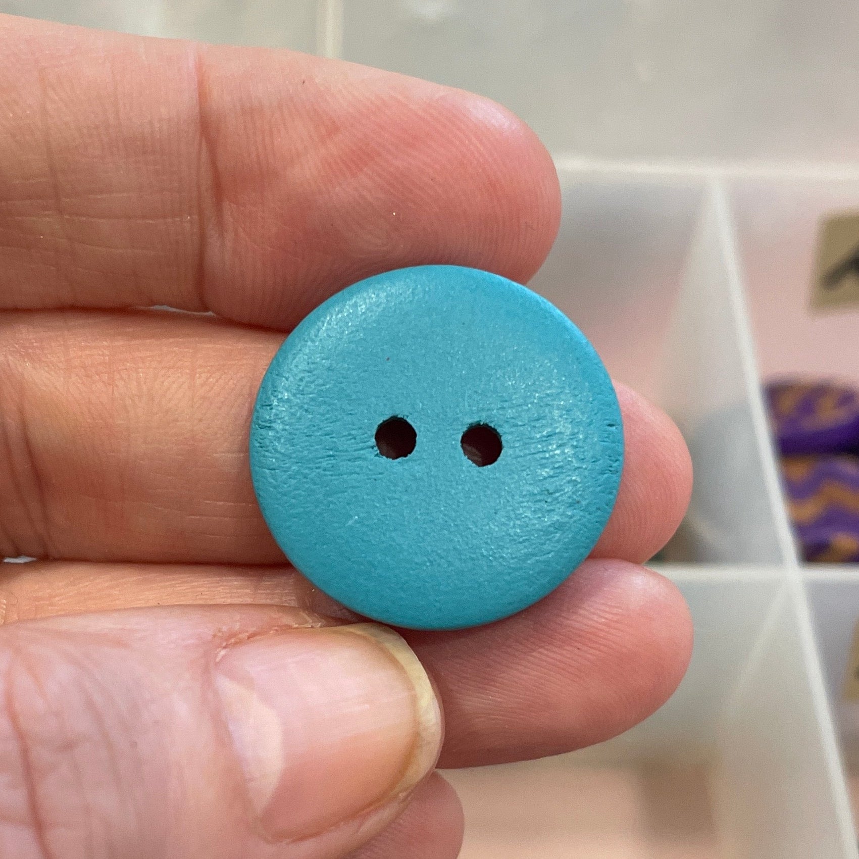 Hand holding a blue button with a collection of buttons in the background