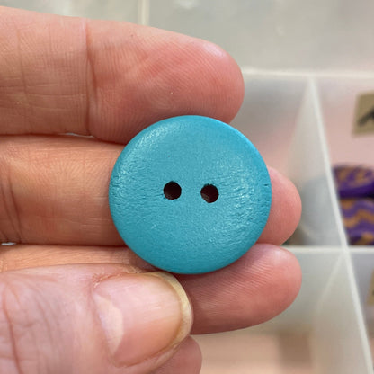 Hand holding a blue button with a collection of buttons in the background
