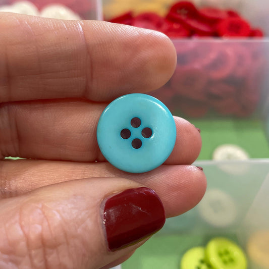 Hand holding a blue button with a container of colorful buttons in the background