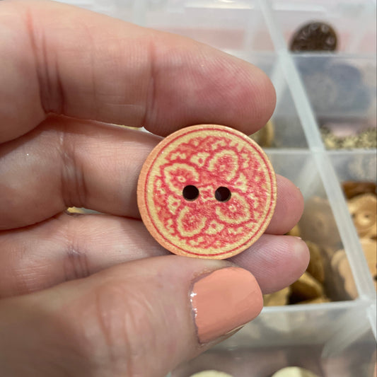 Hand holding a round decorative button with intricate design, set against a background of similar buttons.