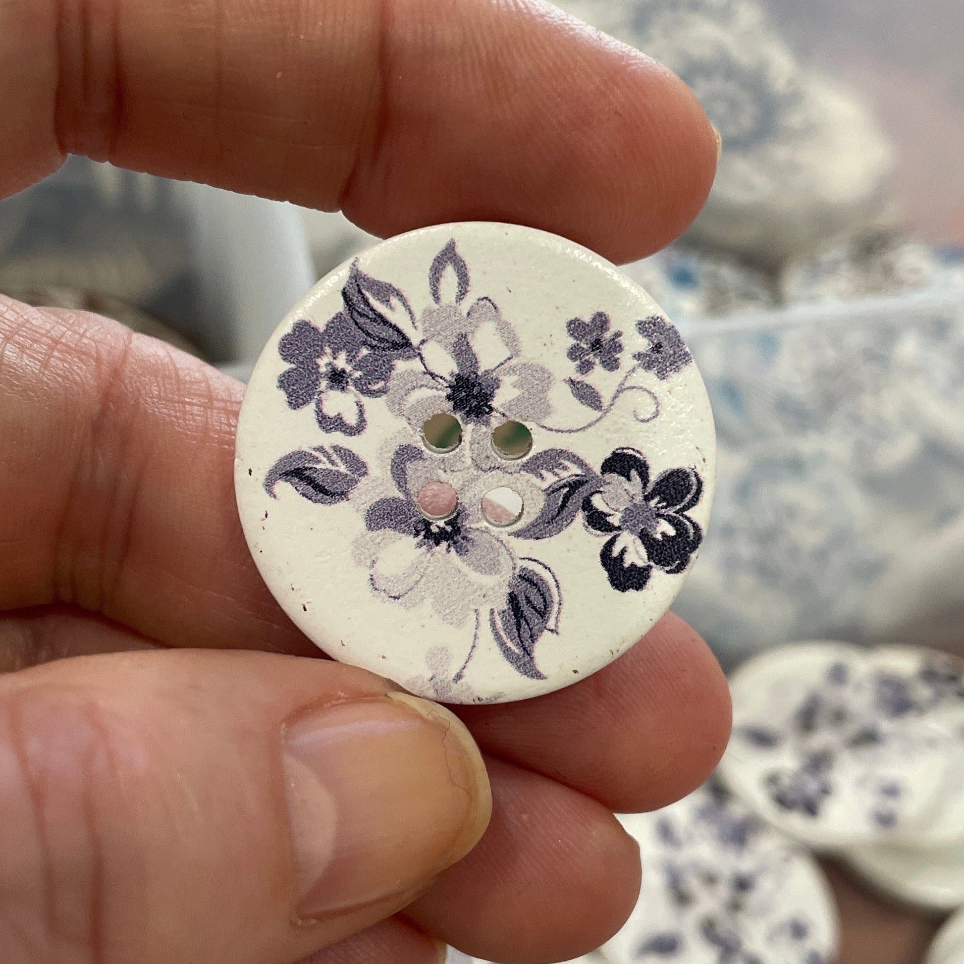 Hand holding a floral-patterned button with a blurred background of more buttons.