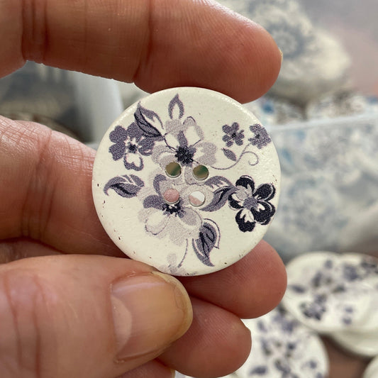 Hand holding a floral-patterned button with a blurred background of more buttons.