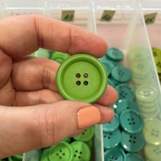Hand holding a green button with a container of green buttons in the background