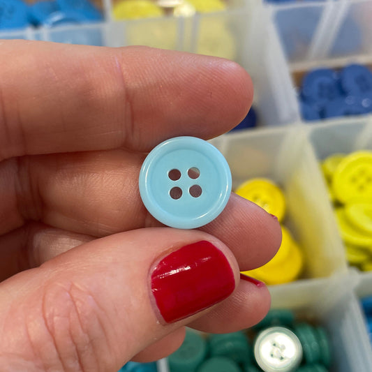 Hand holding a blue button with a container of buttons in the background
