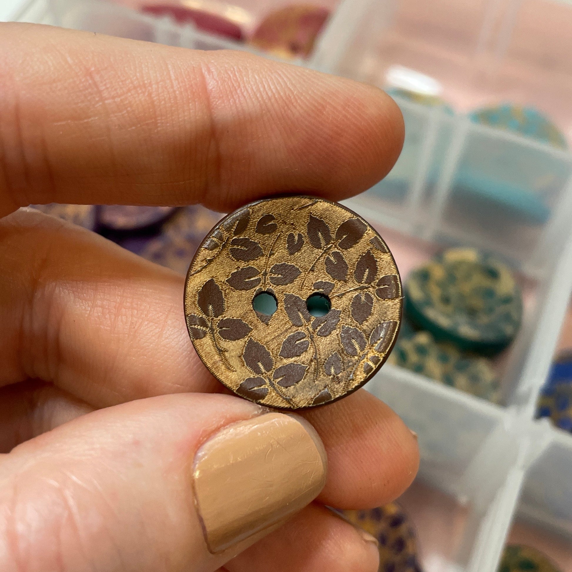 Hand holding a floral-patterned button with a container of buttons in the background
