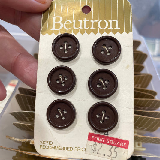 Pack of brown buttons with a Beutron label held by a hand.