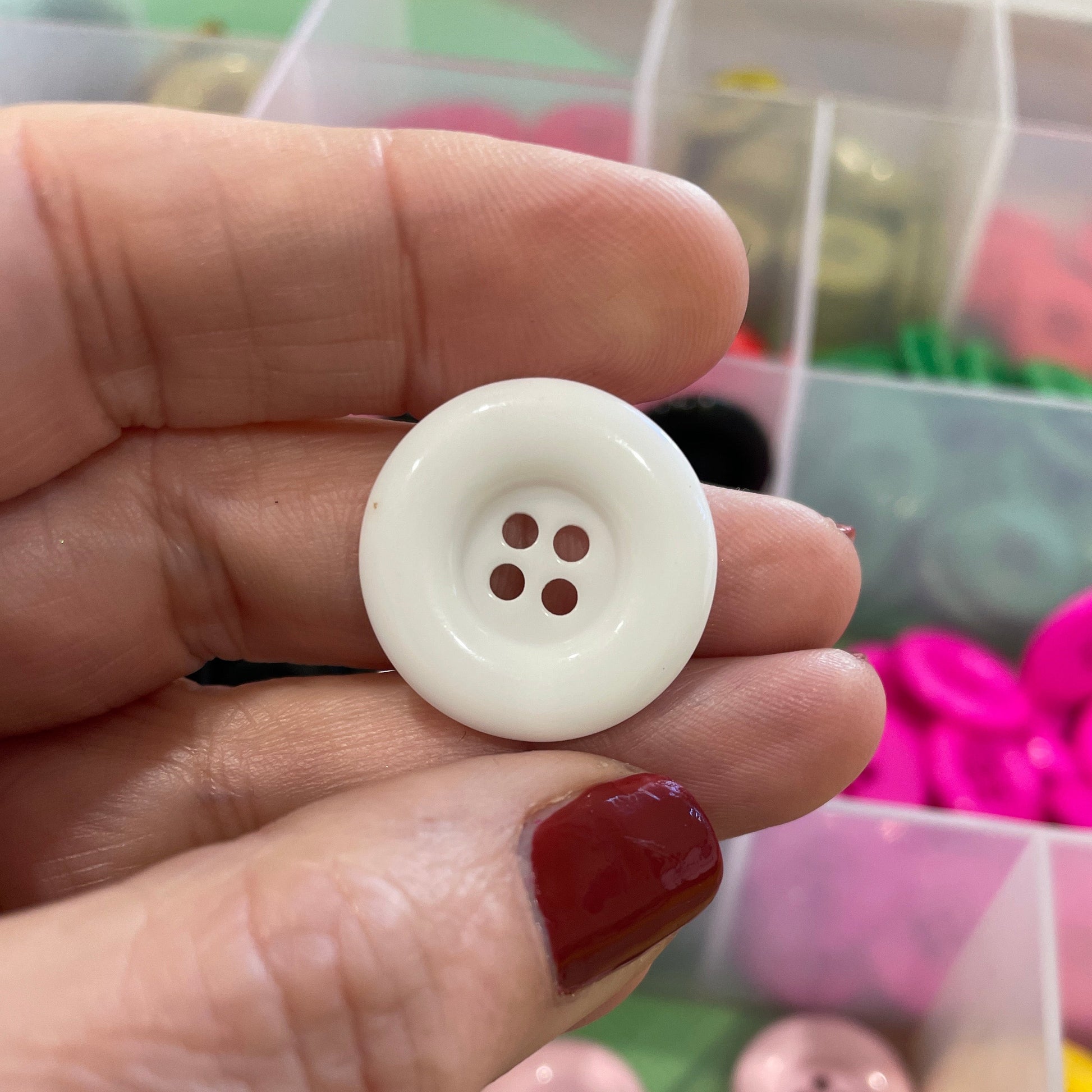Hand holding a white button with a container of colorful buttons in the background