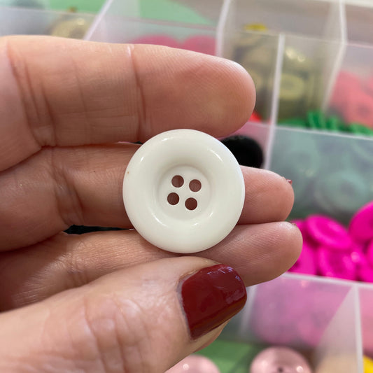 Hand holding a white button with a container of colorful buttons in the background