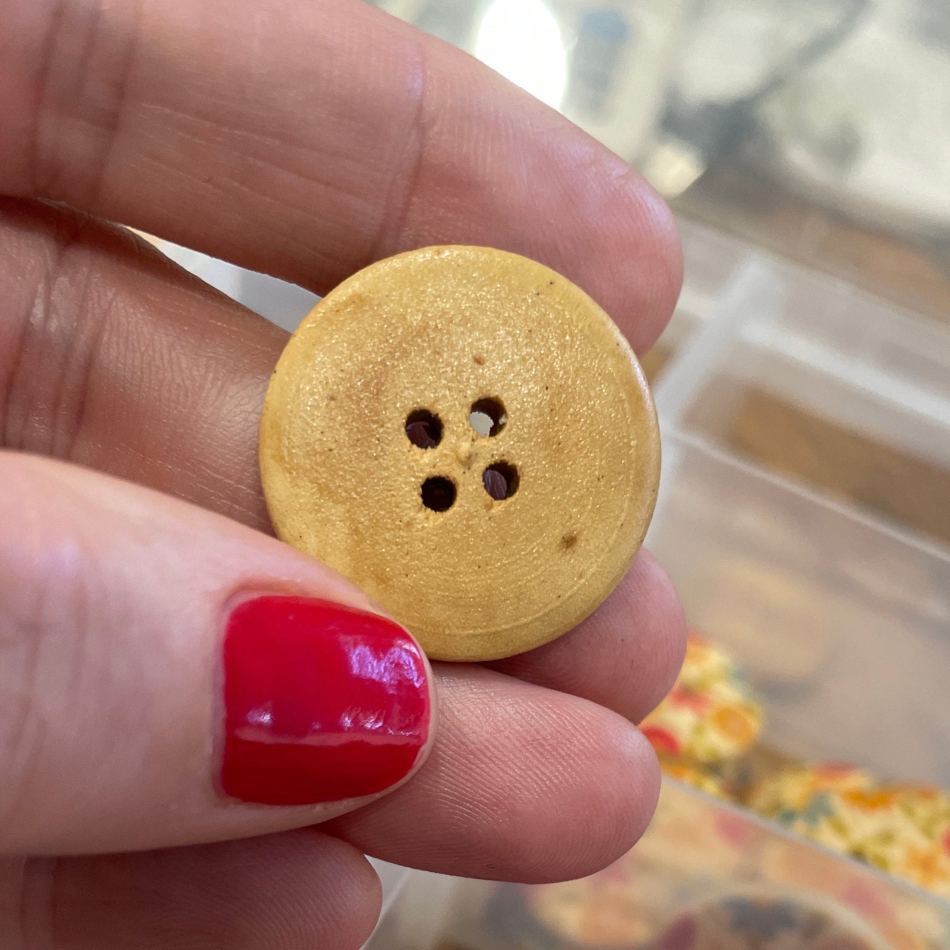 Hand holding a yellow button with a blurred background of colorful buttons in a container