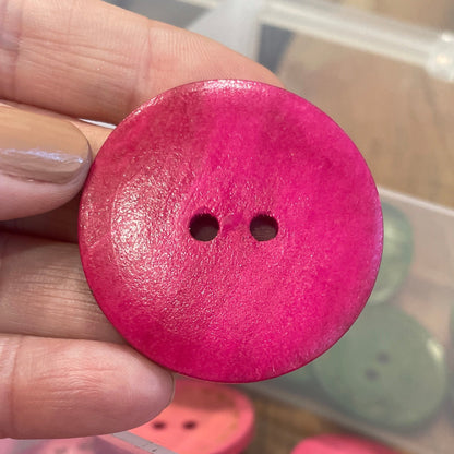 Hand holding a pink button with a container of pink buttons in the background