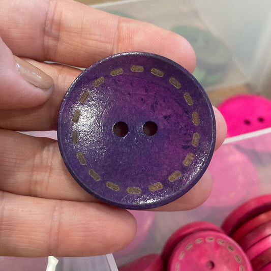 Purple button held by a hand with pink buttons in the background