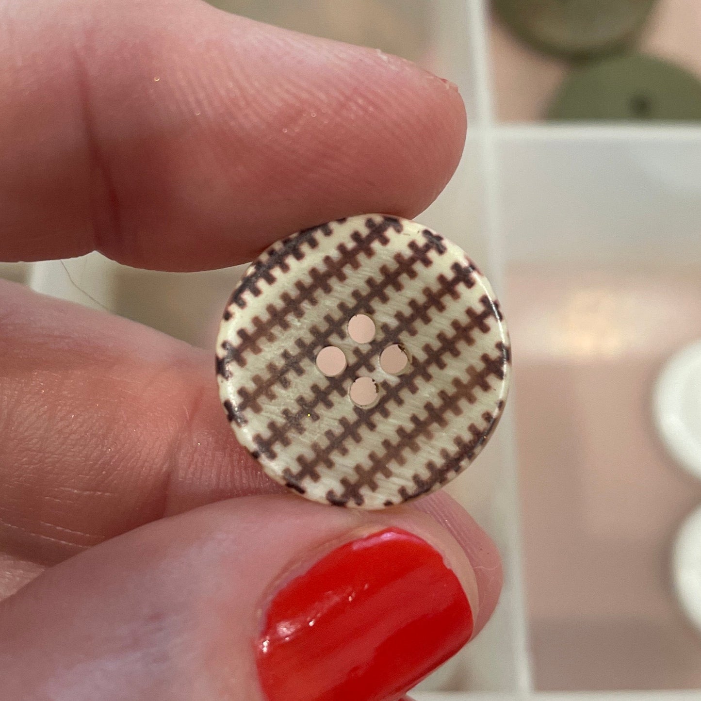 Hand holding a round button with a houndstooth pattern in front of a button collection.